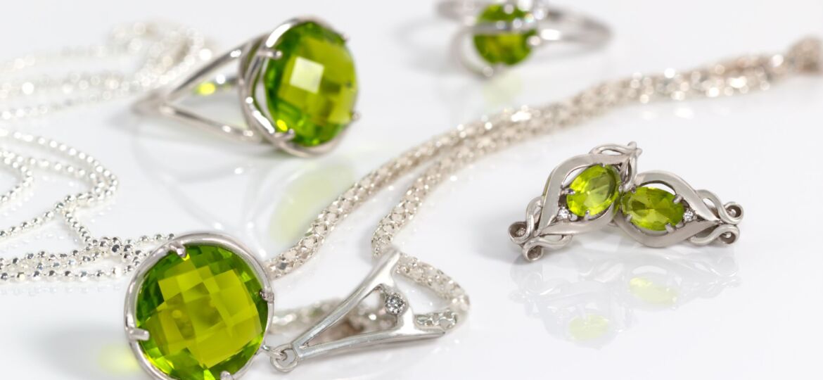 Image of Close-up beauty silver earrings and pendant with peridot on background chain and rings on white acrylic desk.