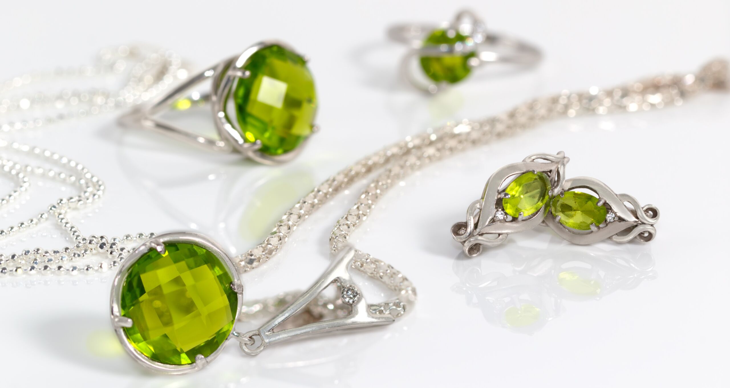 Image of Close-up beauty silver earrings and pendant with peridot on background chain and rings on white acrylic desk.
