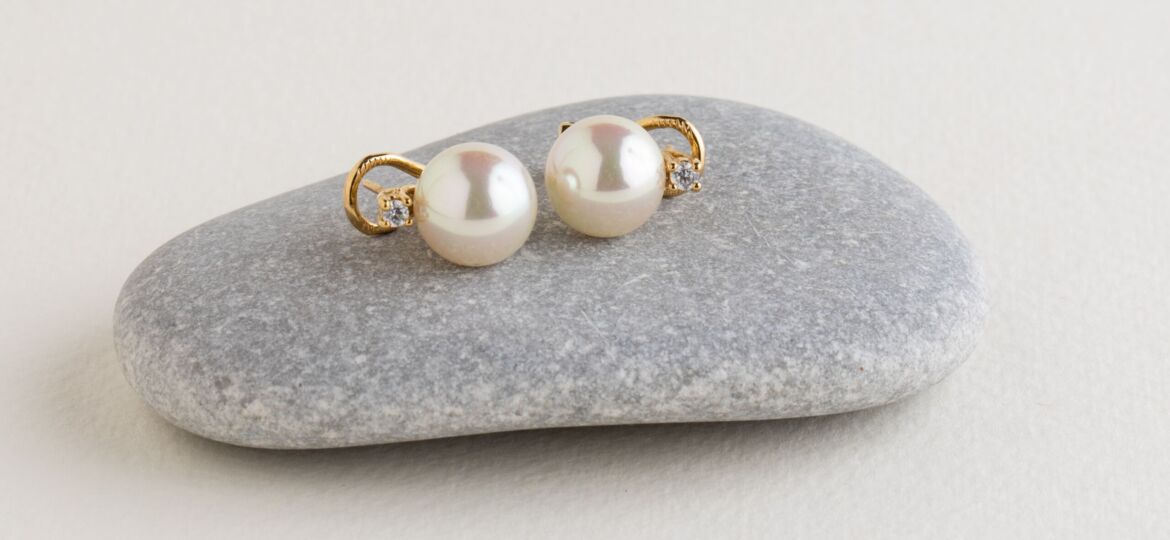 Image of White pearl earrings in gold on a gray stone