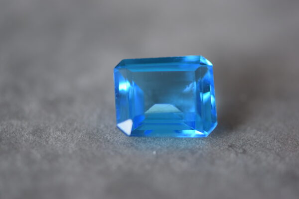 a 12 carat swiss blue topaz gem on a grey surface in sunlight