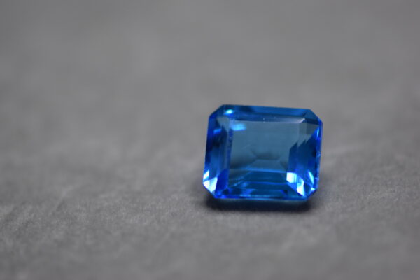 a 12 carat swiss blue topaz gem on a grey surface in white light